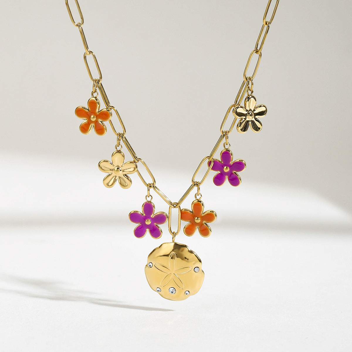 Bright lighting shows purple and orange flower pendants with a gold sand dollar charm on a statement chain.