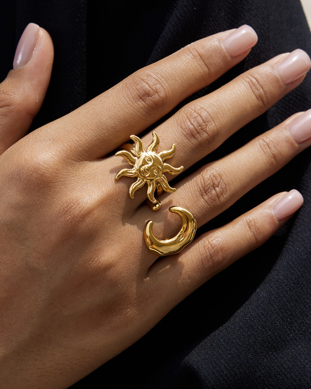 Gold sun and moon ring on a hand against a dark background
