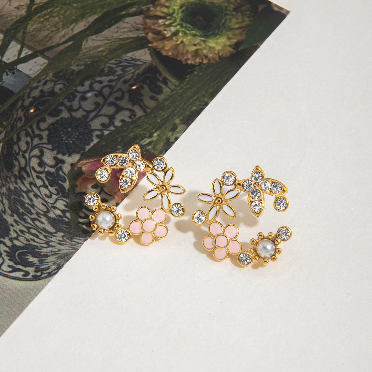 Pair of floral earrings with gold, pink, and pearl details on a white surface.