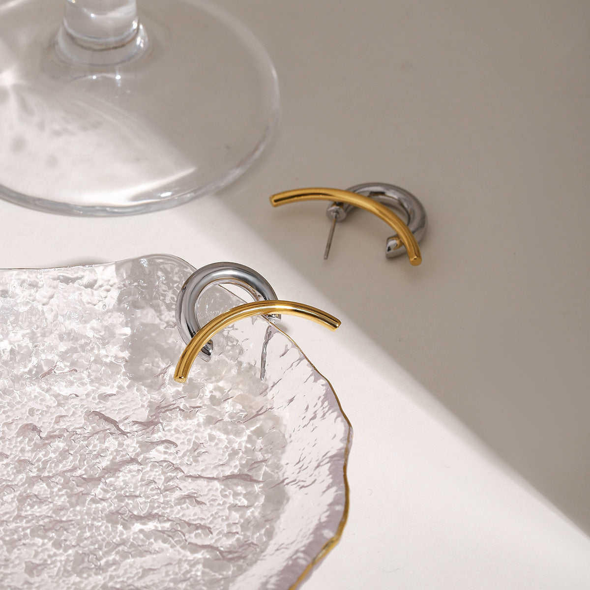 Gold and silver waterproof hoop earrings on textured glass plate