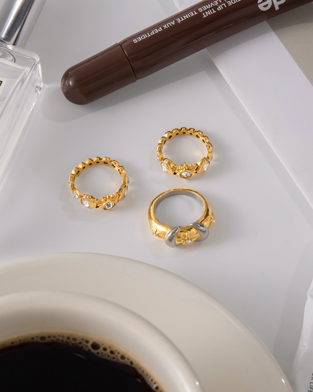 Three gold rings on a white surface with a pen and coffee cup in the background.
