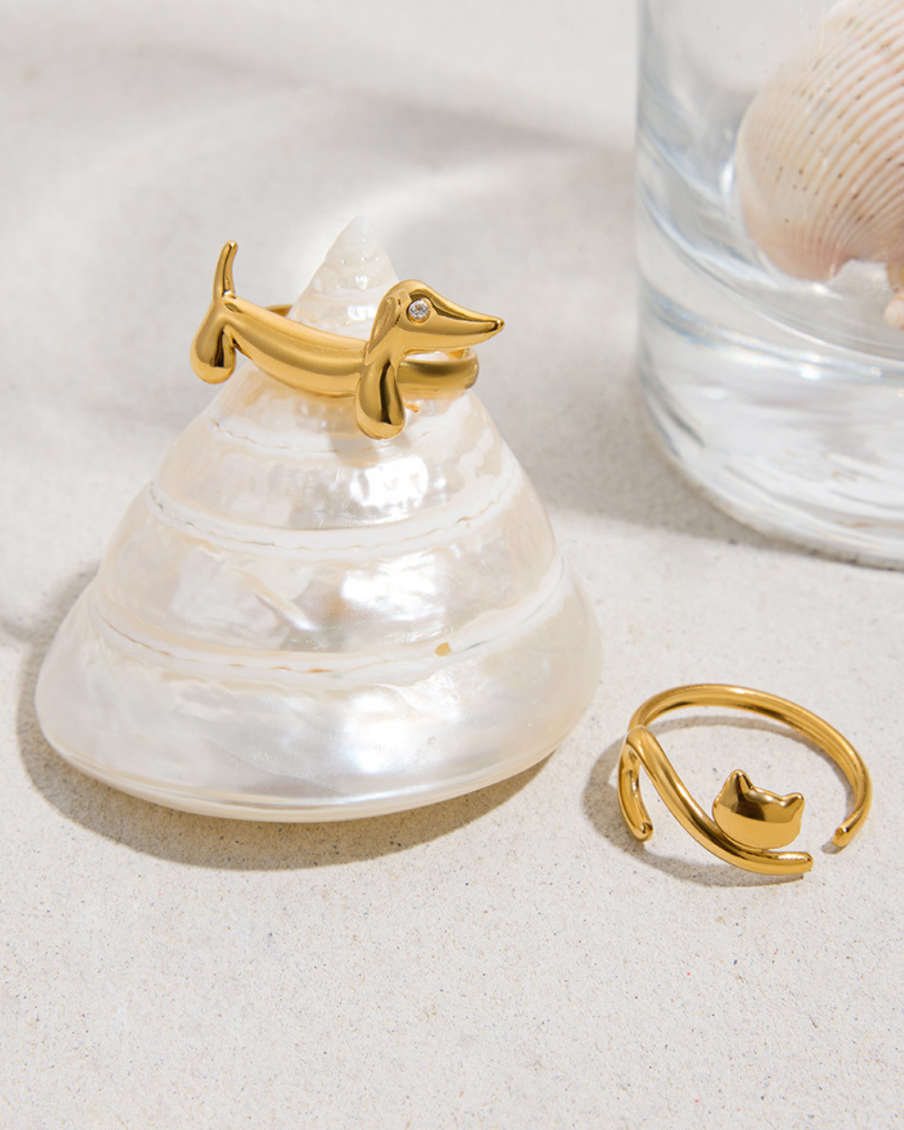 Gold dog-shaped ring on a shell with a glass container and shell in the background