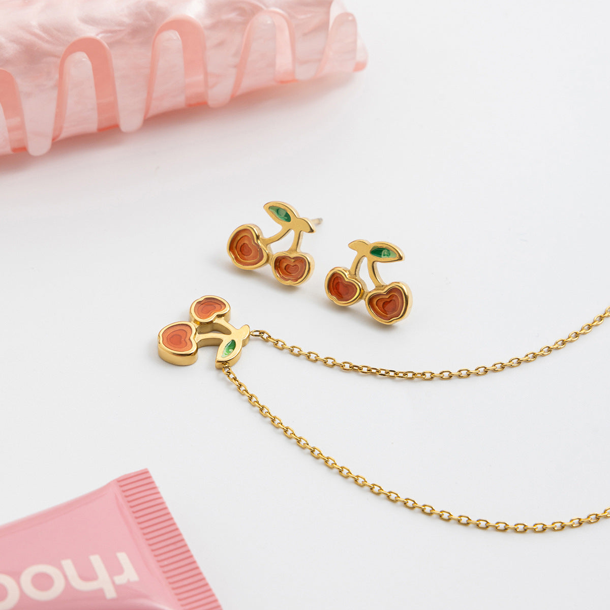 Cherry-themed gold earrings and necklace on a white background with pink tissue paper.