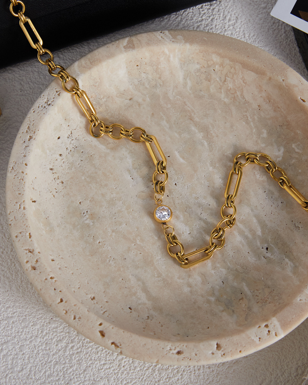 Gold chain necklace with a small round gemstone on a beige stone surface