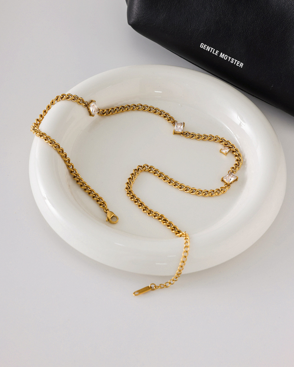 Gold chain necklace on a white dish with 'Gentle Monster' bag in the background