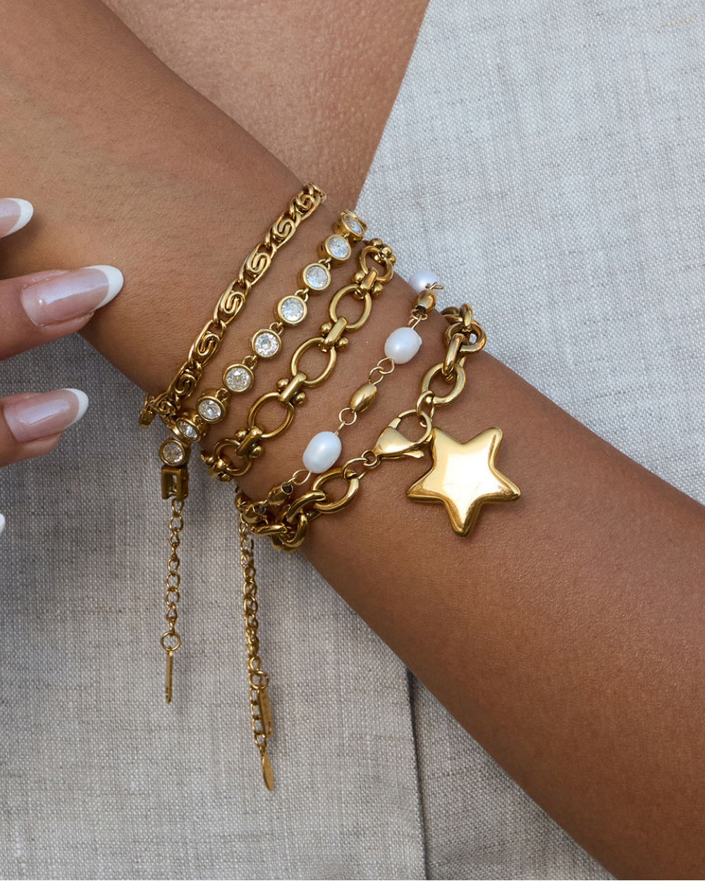 Gold bracelets with various charms on a wrist against a neutral background