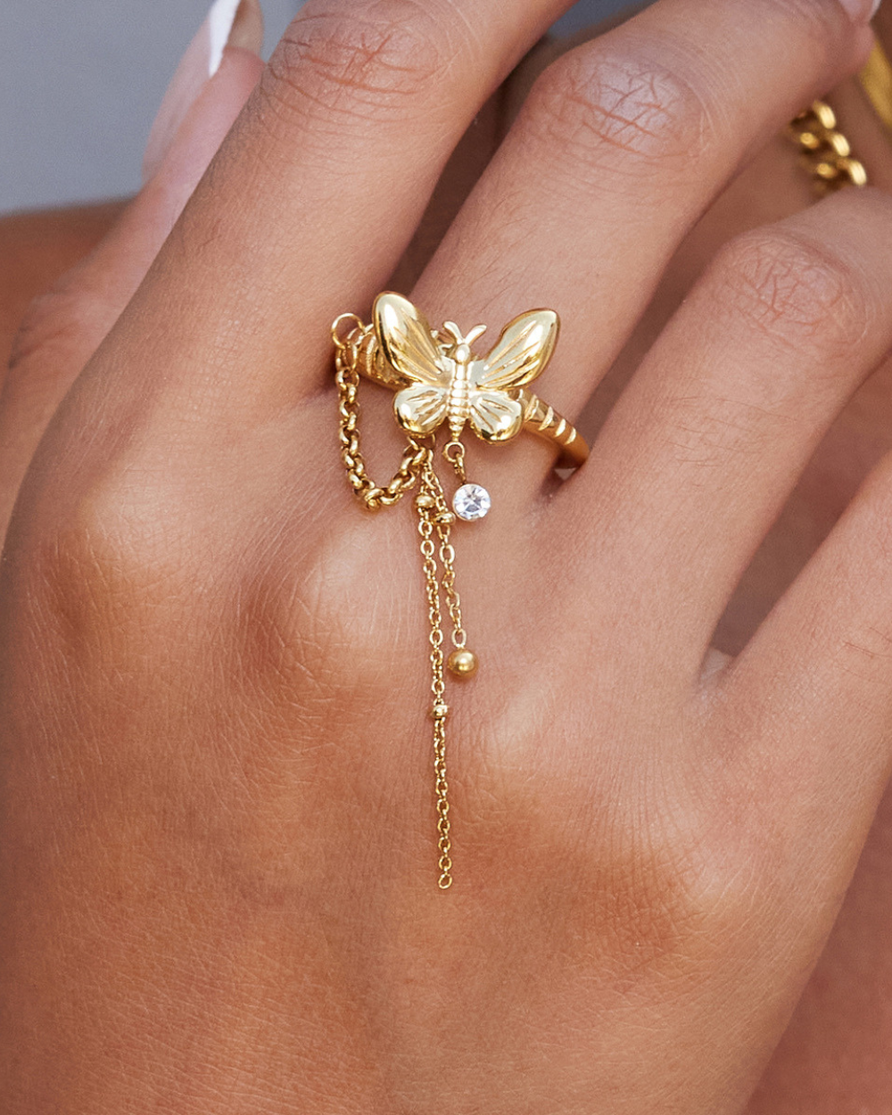 Gold ring with butterfly design and chain on a hand
