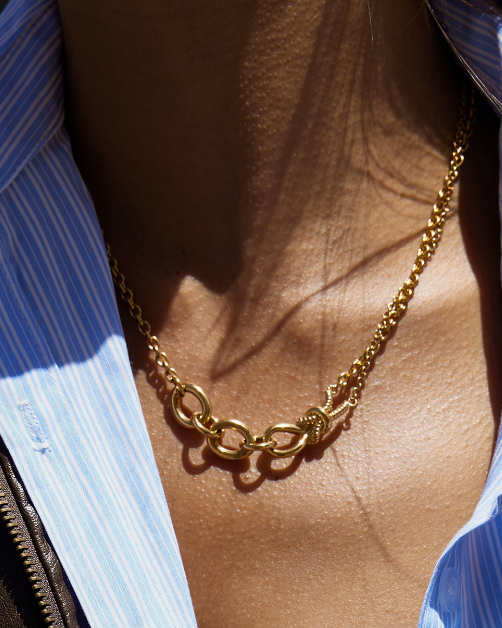 Gold chain necklace on a person wearing a blue striped shirt.