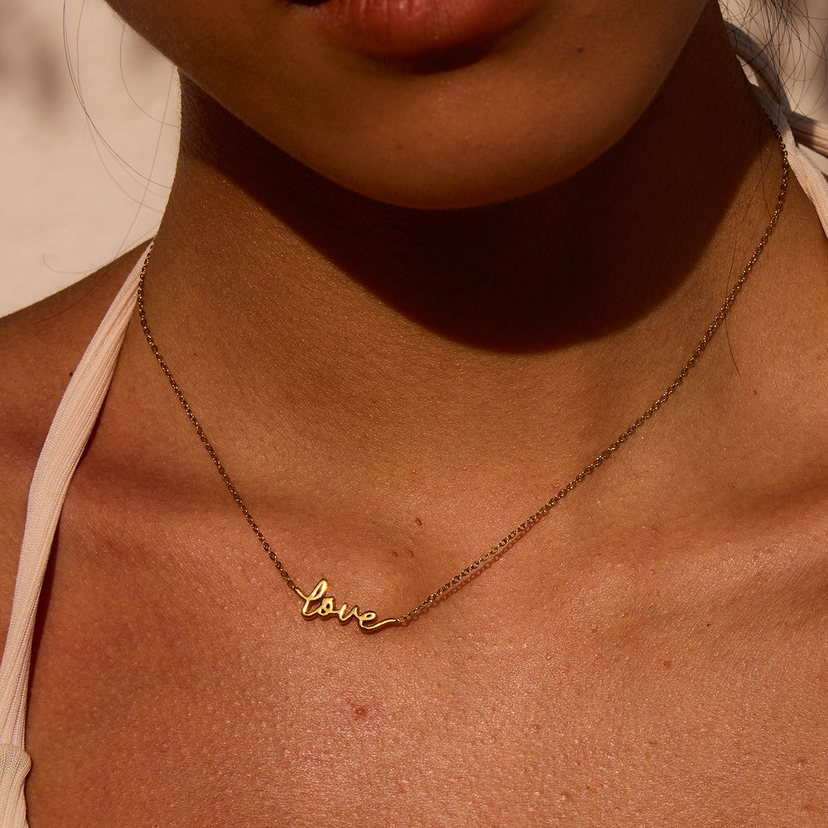 Golden hour close-up of "love" necklace worn with strappy white top