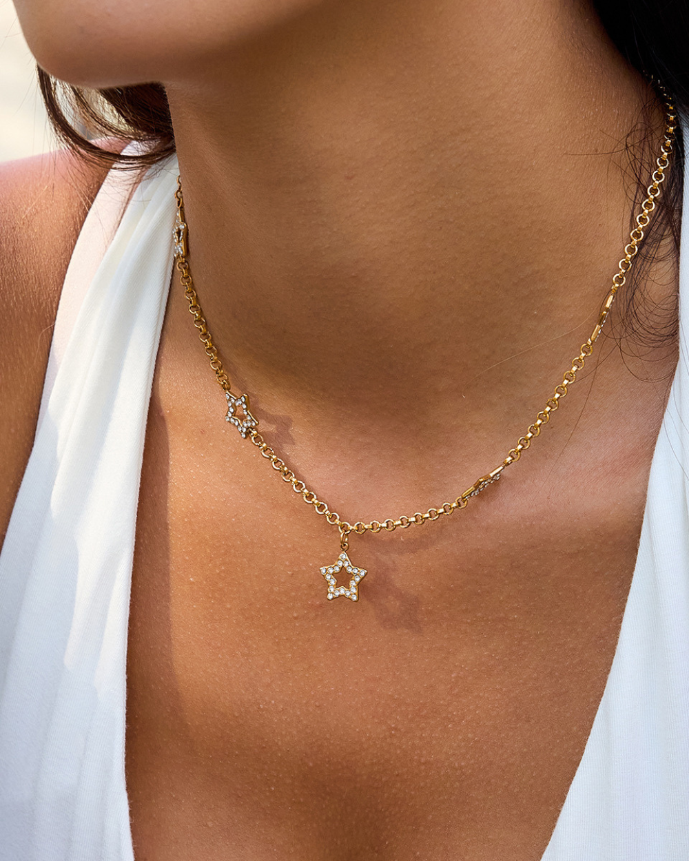 Gold necklace with a star pendant worn by a person in a white top.