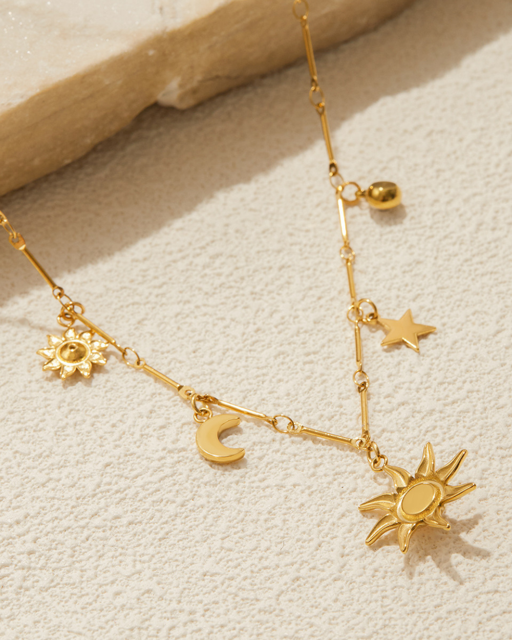 Gold necklace with sun and moon charms on a textured beige surface