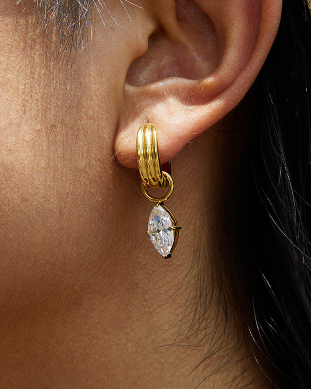 Gold hoop earring with a marquise-shaped diamond on an ear.