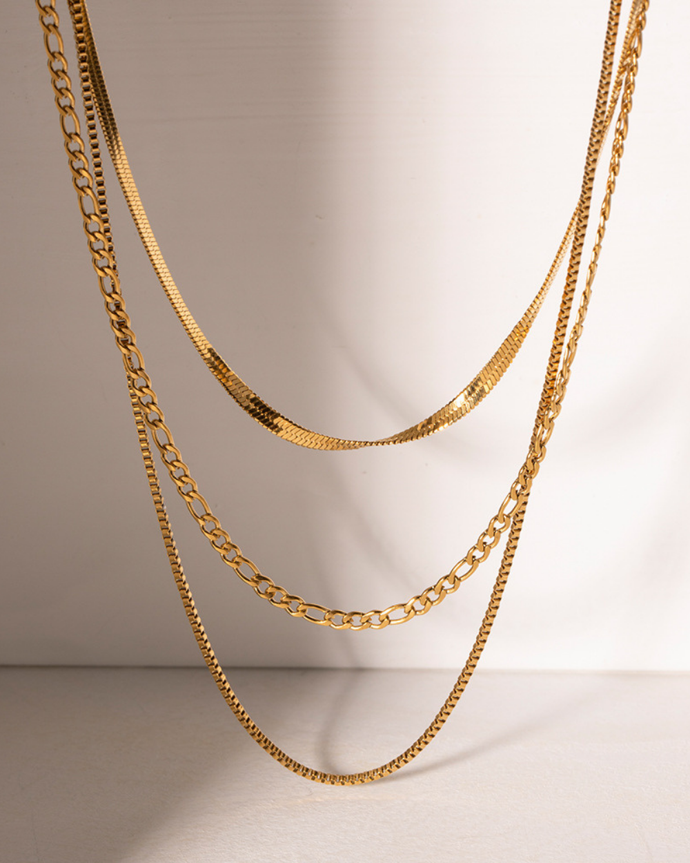 Three gold chain necklaces on a light gray background