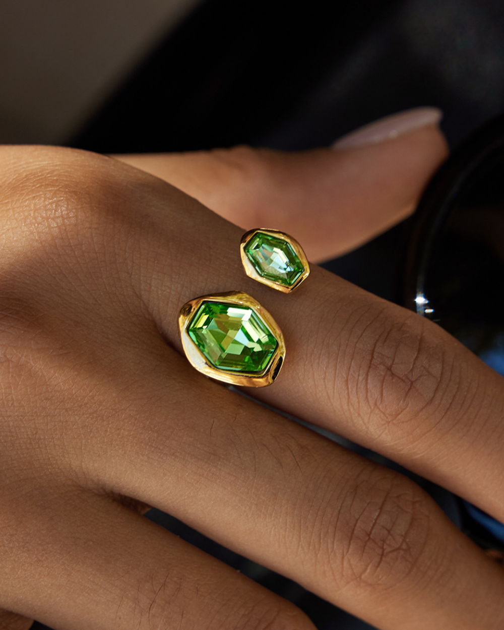 Green gemstone earrings on a person's hand with a dark background