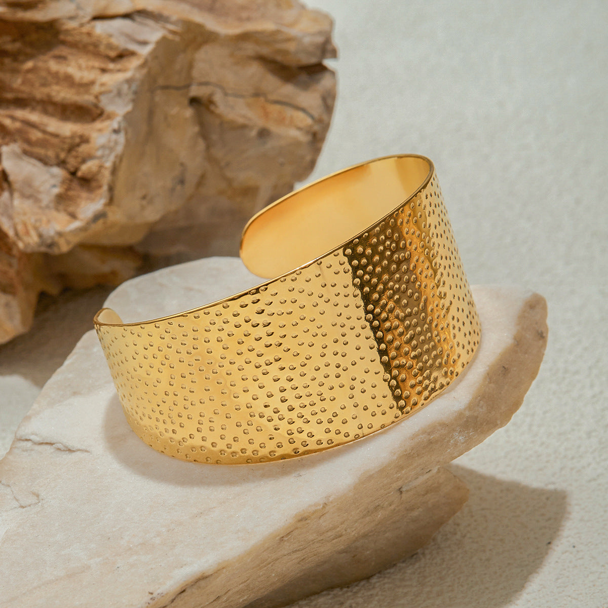 Gold bracelet with textured surface on a stone surface