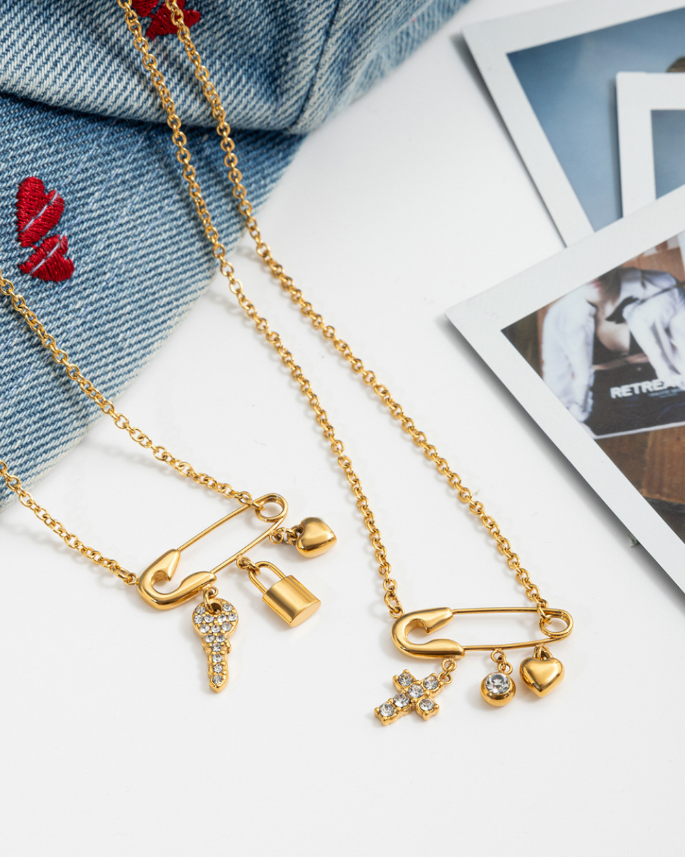 Gold necklaces with charms on a white surface with denim fabric and photos in the background