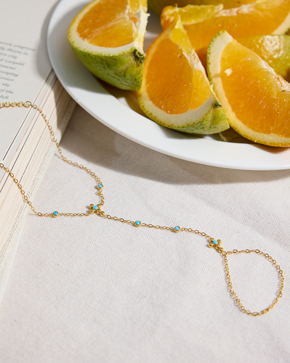 Gold necklace with turquoise stones on a white surface with sliced oranges and limes.