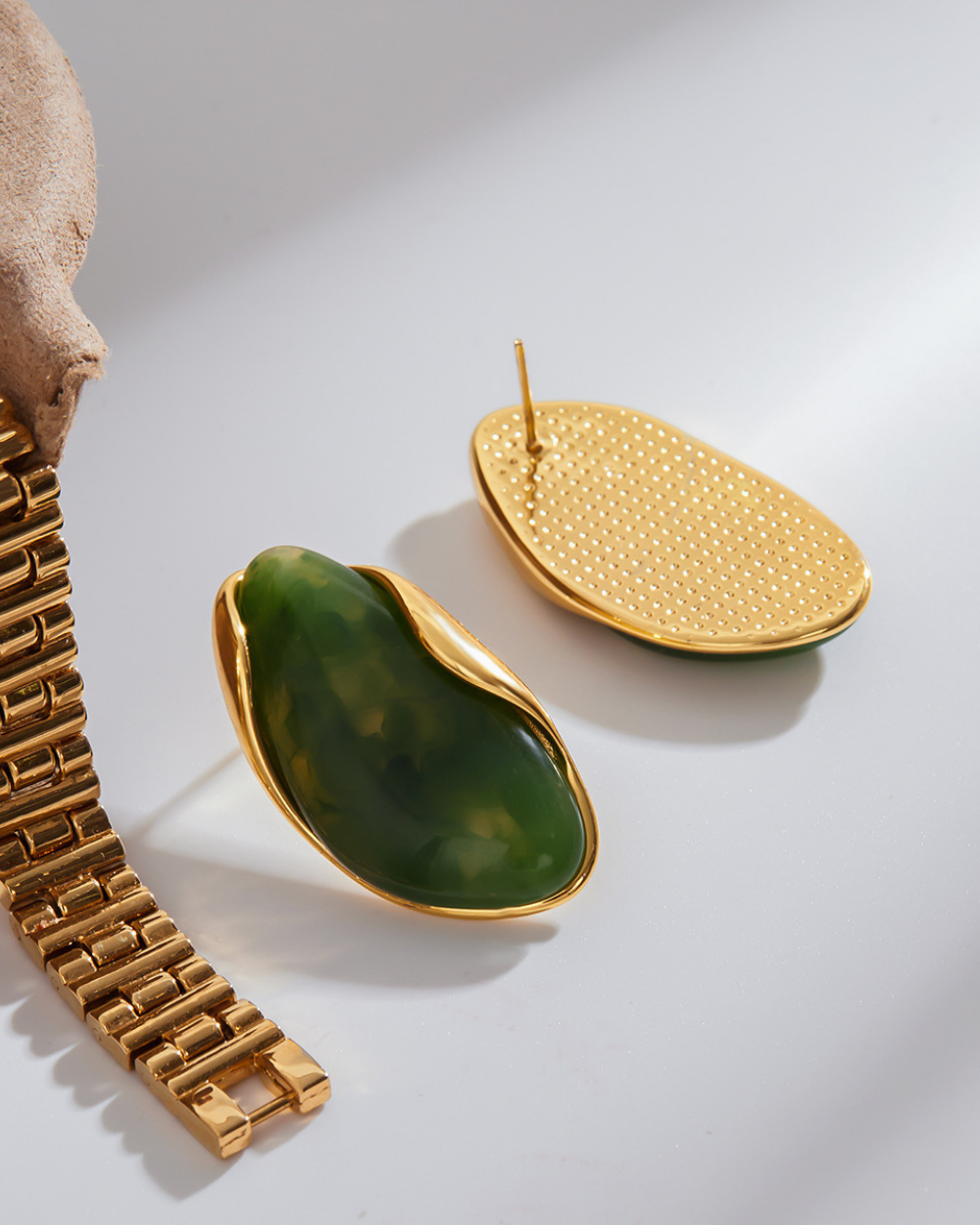 Gold and green earrings on a light gray background