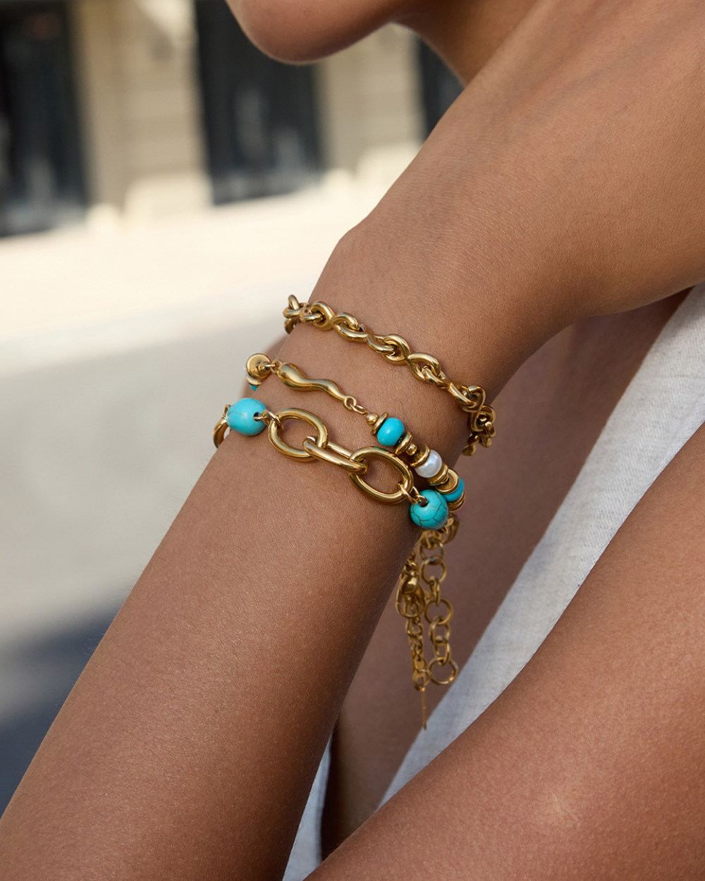 Gold chain bracelet with turquoise beads on a wrist against a blurred background
