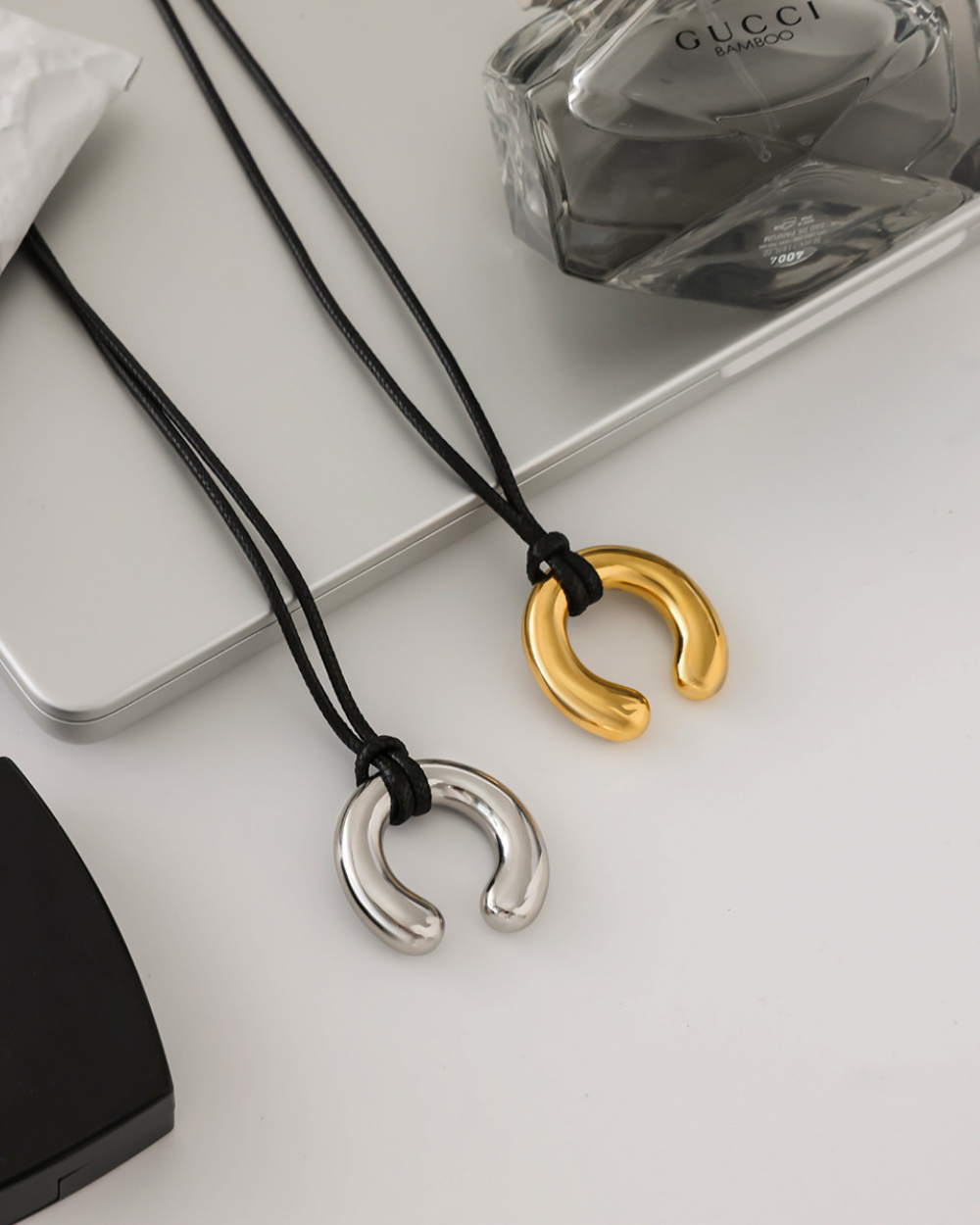 Two necklaces with horseshoe-shaped pendants, one gold and one silver, on a white surface.