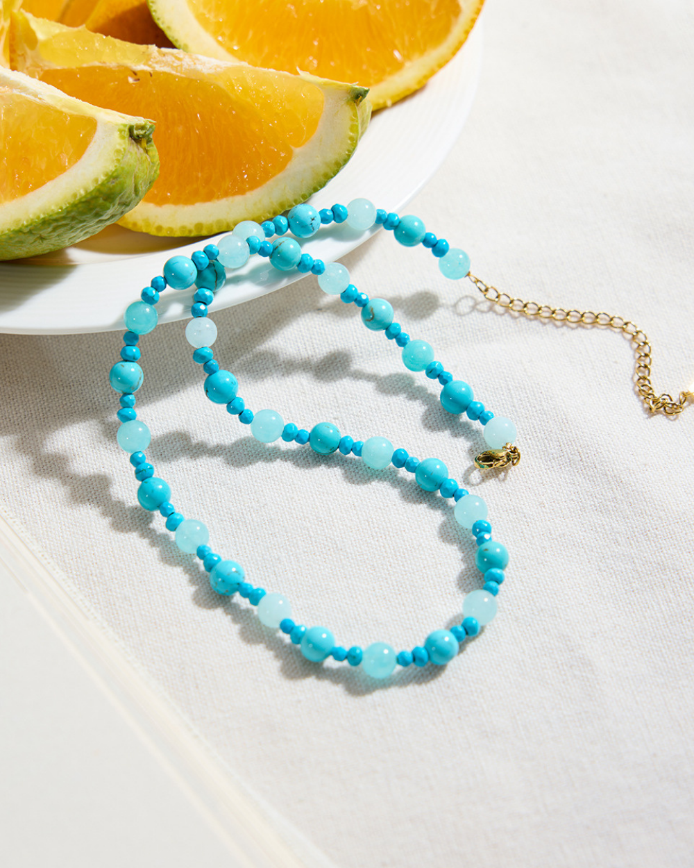 Turquoise beaded necklace on a white surface with sliced oranges in the background