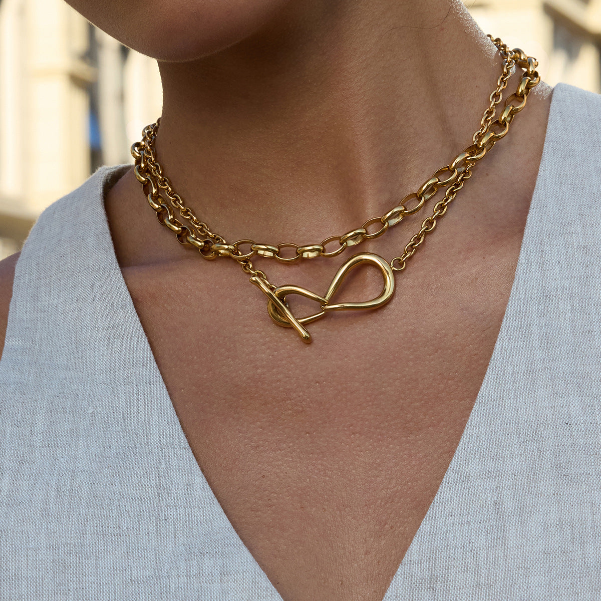 Gold chain necklace with a heart clasp worn by a person in a light blue top.