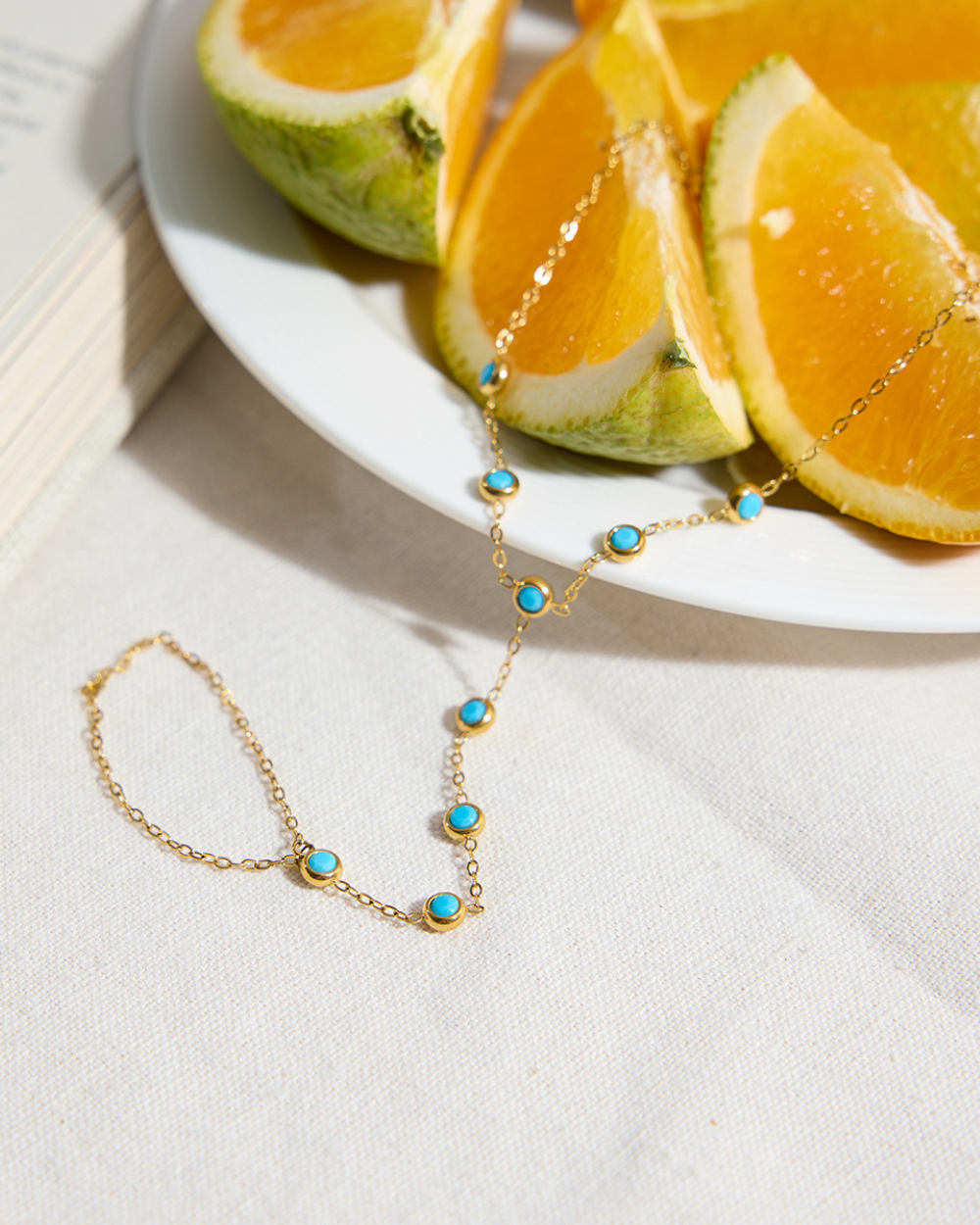 Gold necklace with turquoise stones on a white surface with orange slices in the background
