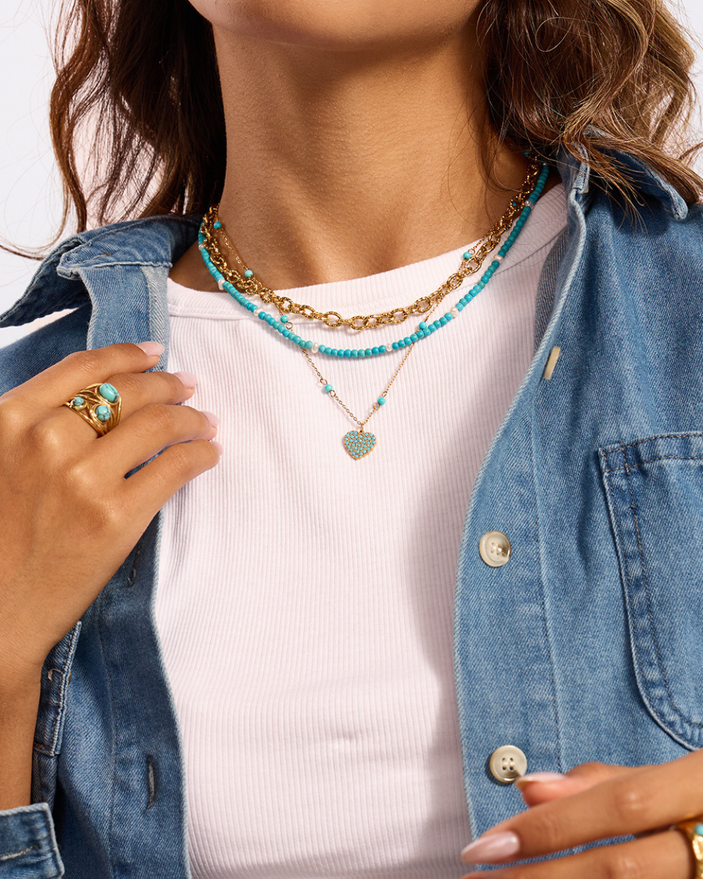 Person wearing multiple necklaces with a denim jacket and white shirt