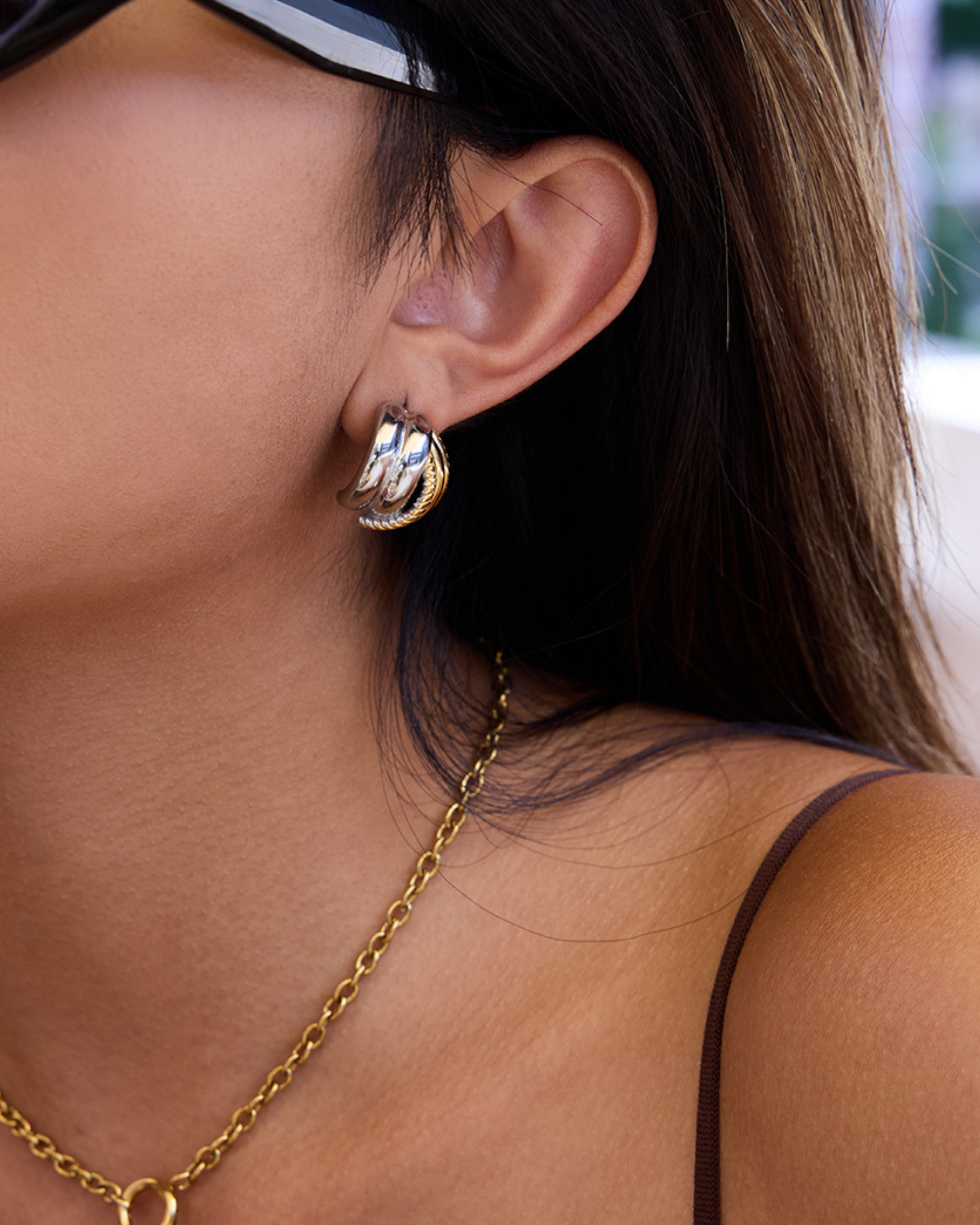 Close-up of a person wearing gold hoop earrings and a gold chain necklace.