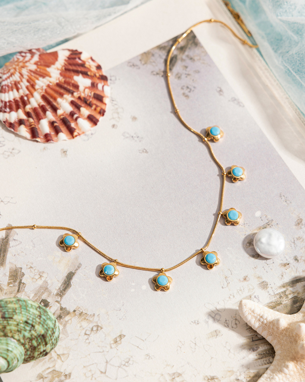 Gold necklace with turquoise stones on a sandy surface with shells