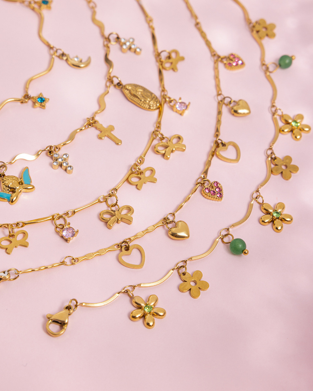 Gold necklaces with various charms on a pink background