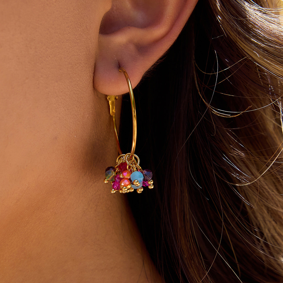 Gold hoop earring with colorful beads worn by a person