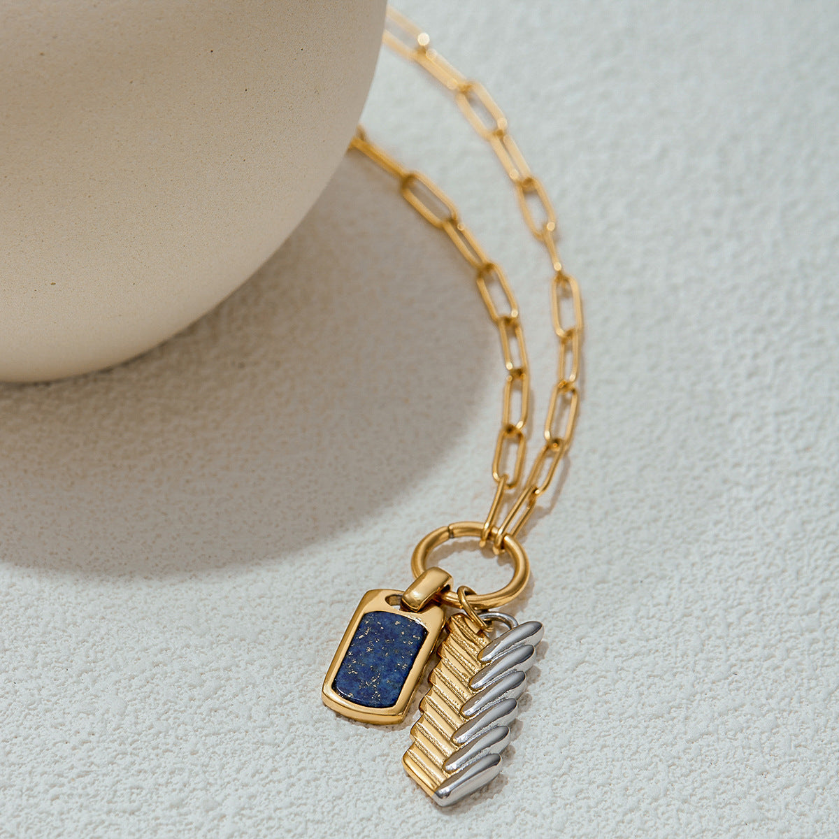 Flat-lay shot of dual-tone pendant necklace with rectangular lapis charm and metallic feather