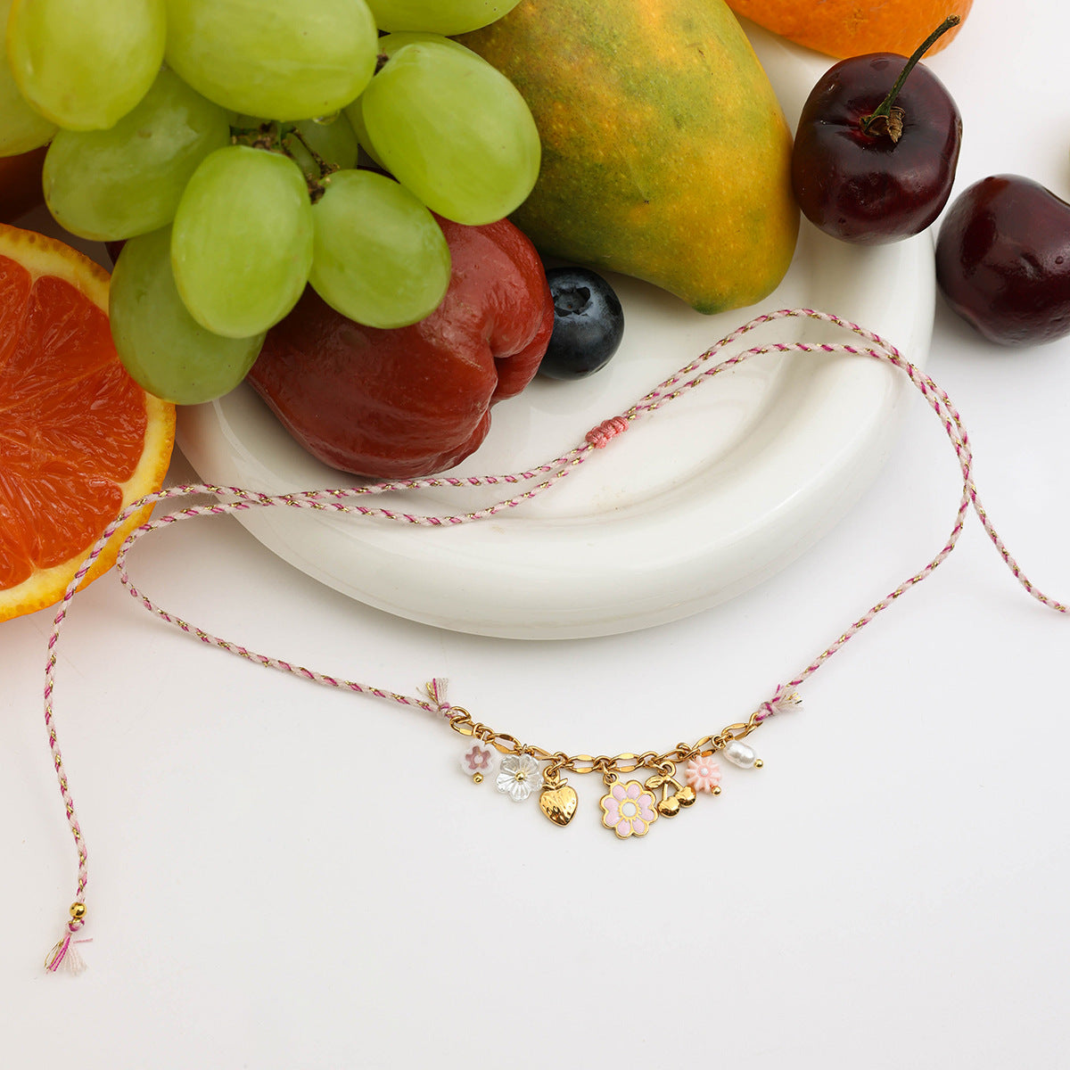 Close-up of pink woven necklace with gold flower, heart, and cherry charms