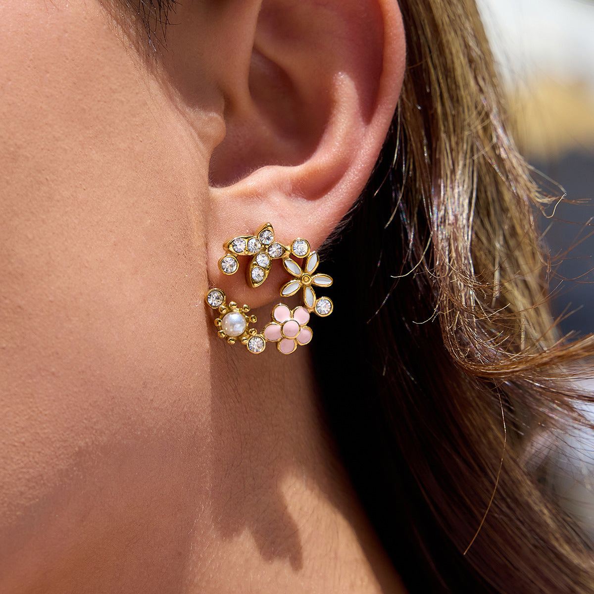 Close-up of a person wearing gold floral earrings with clear stones.