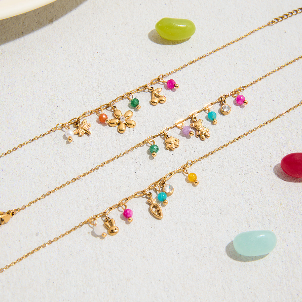 Flat lay of three charm bracelets on sand with colorful candy props