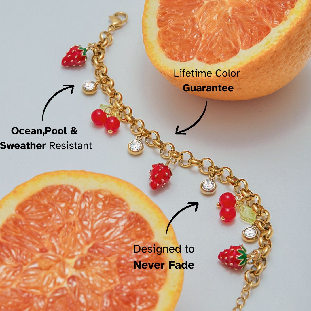 Playful gold fruit bracelet with strawberry and cherry charms styled beside fresh orange