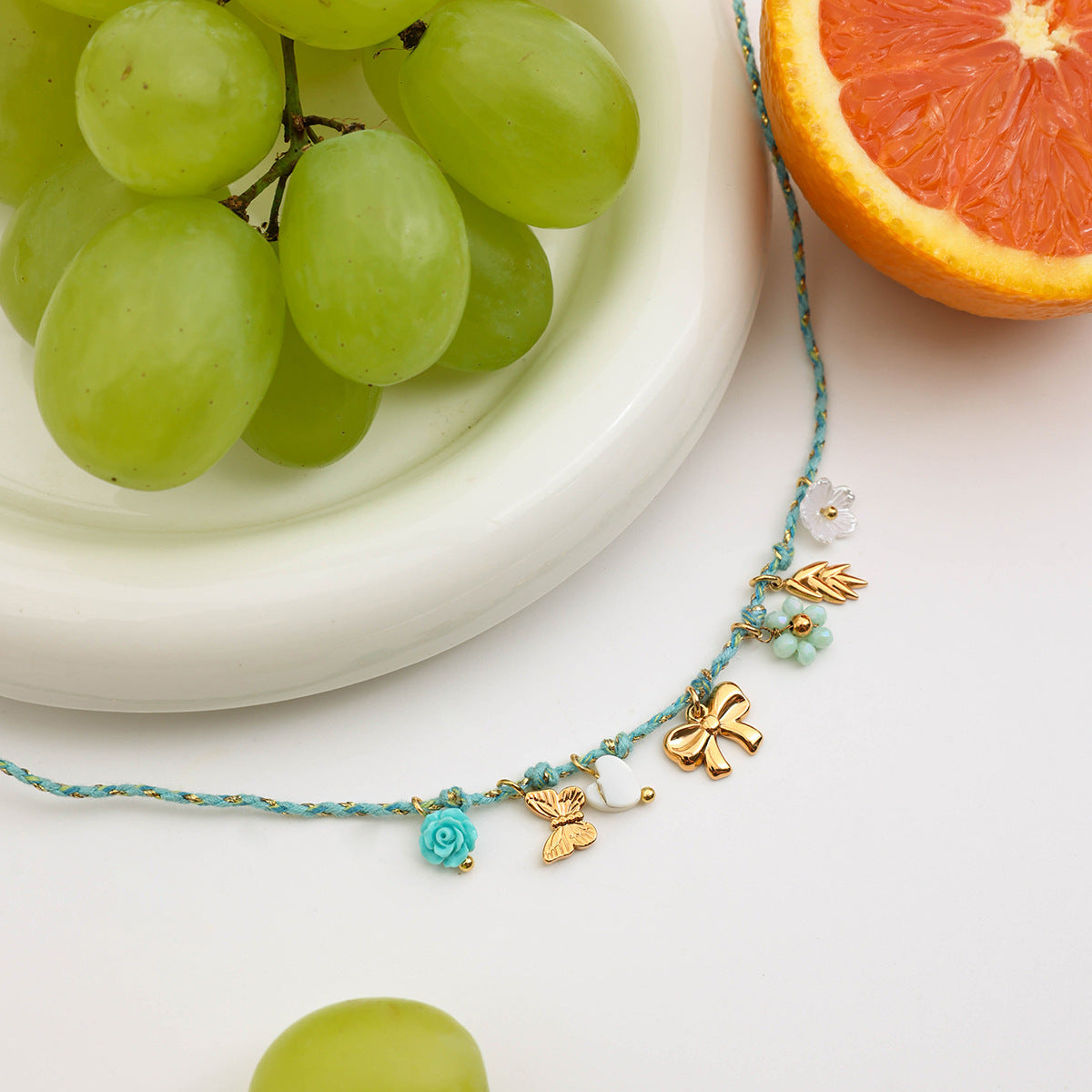 Necklace styled with grapes and citrus fruits, showcasing gold and enamel charms