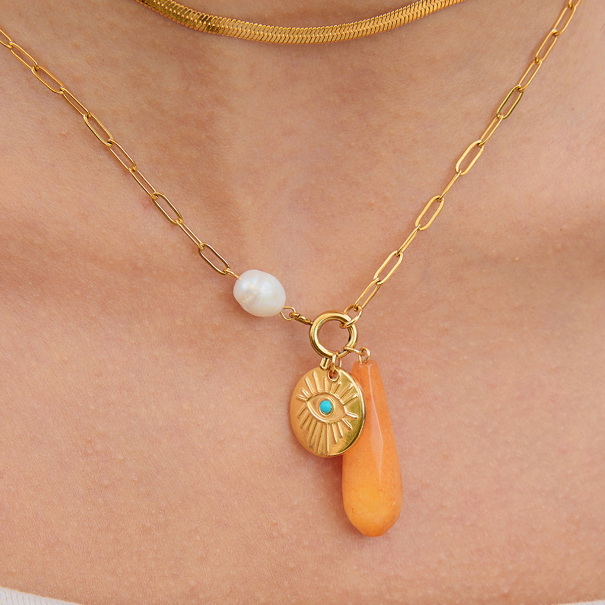 Flat lay of golden necklace with orange teardrop and engraved coin on neutral background