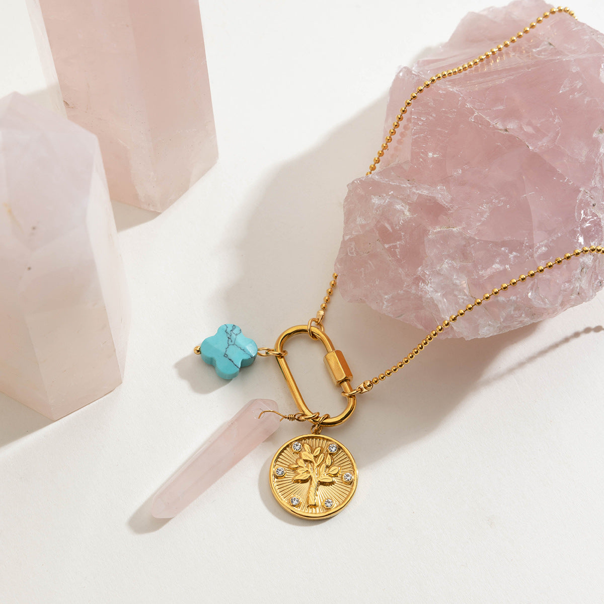 Gold necklace with pink and turquoise stones laid on rose quartz crystals