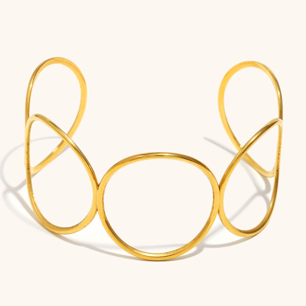 Open bangle bracelet featuring gold teardrop and circular cutout shapes, shown from top angle.