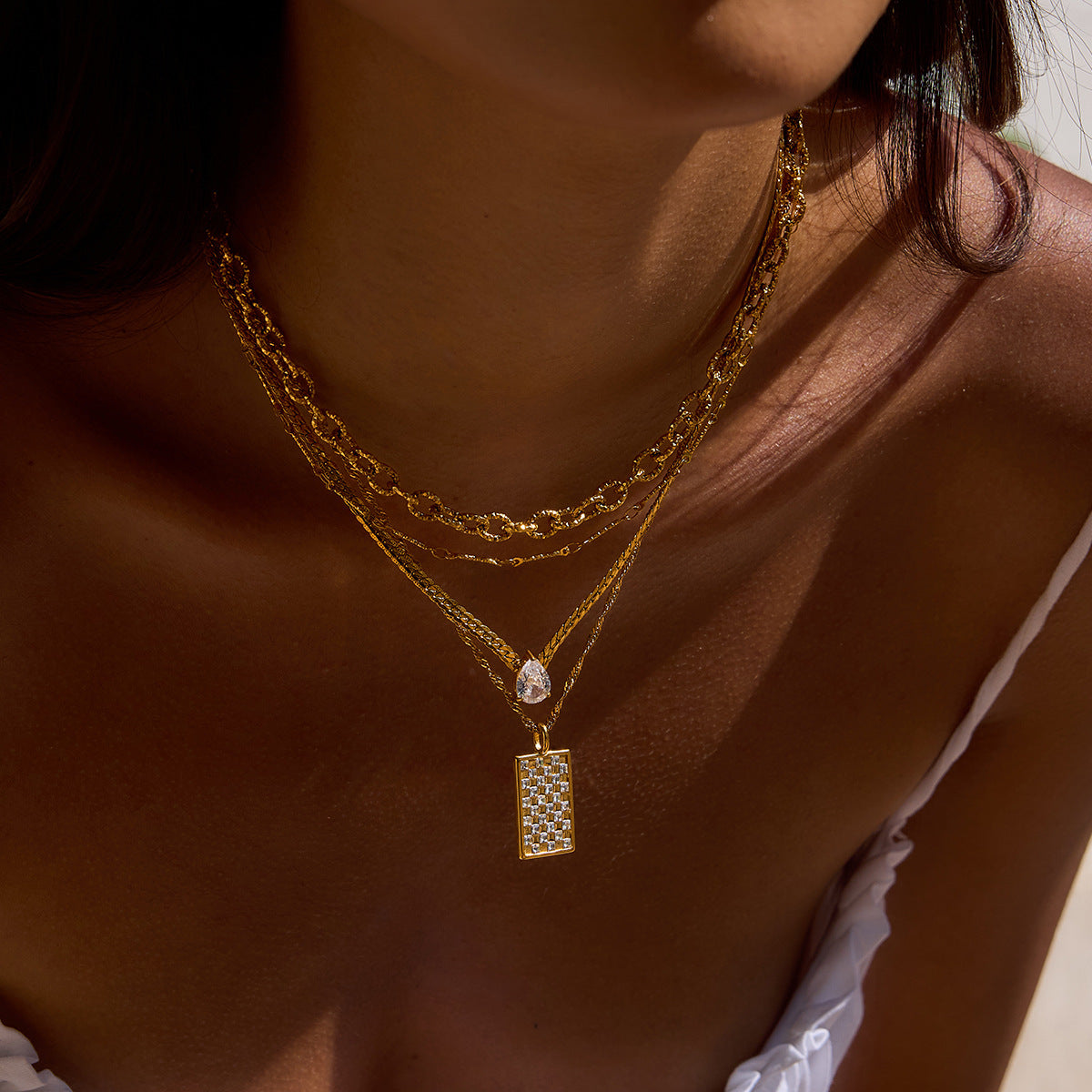 Zoom-in of multiple gold chains with the featured square pendant on model’s neck.
