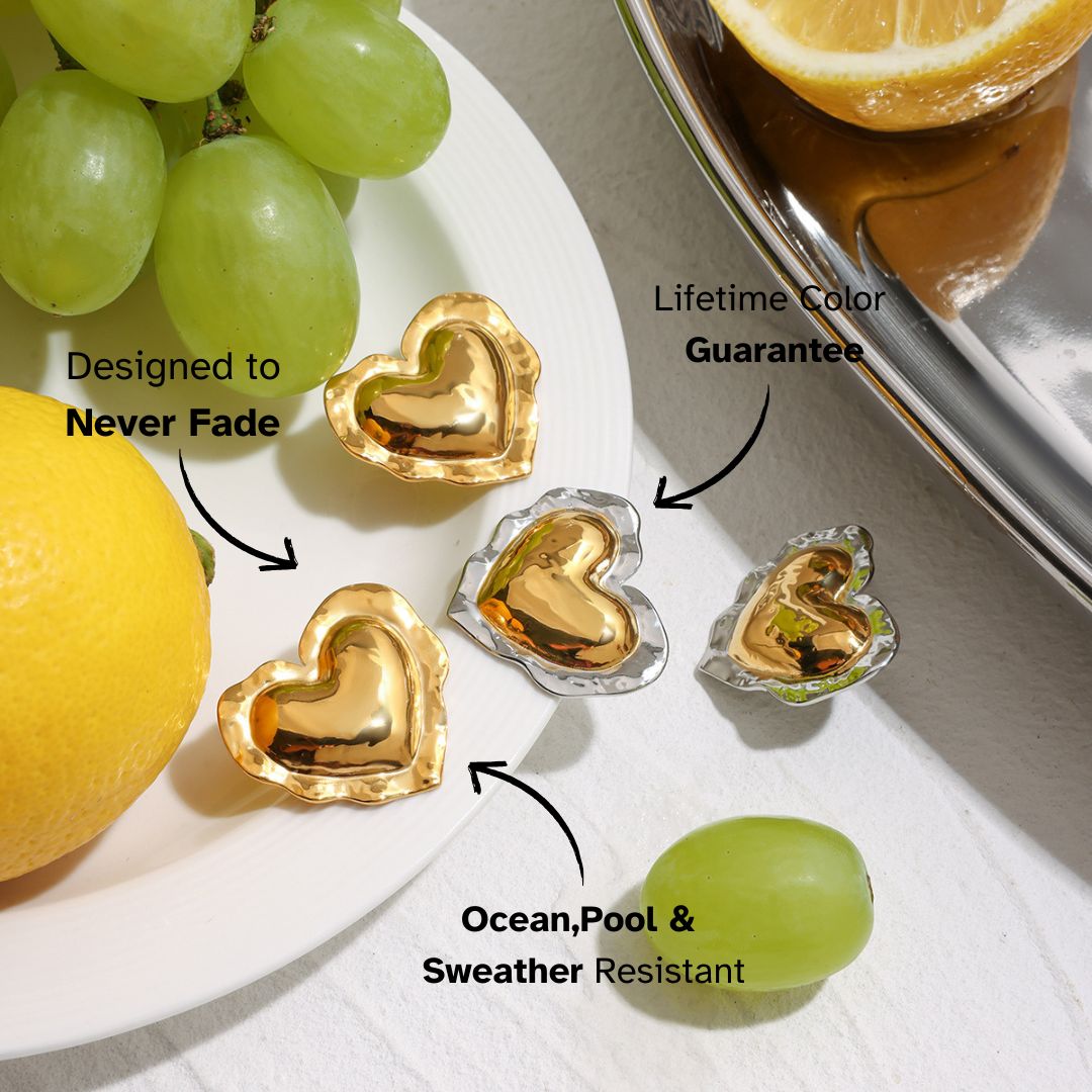 Glossy gold heart earrings styled on a white plate with lemon and grapes