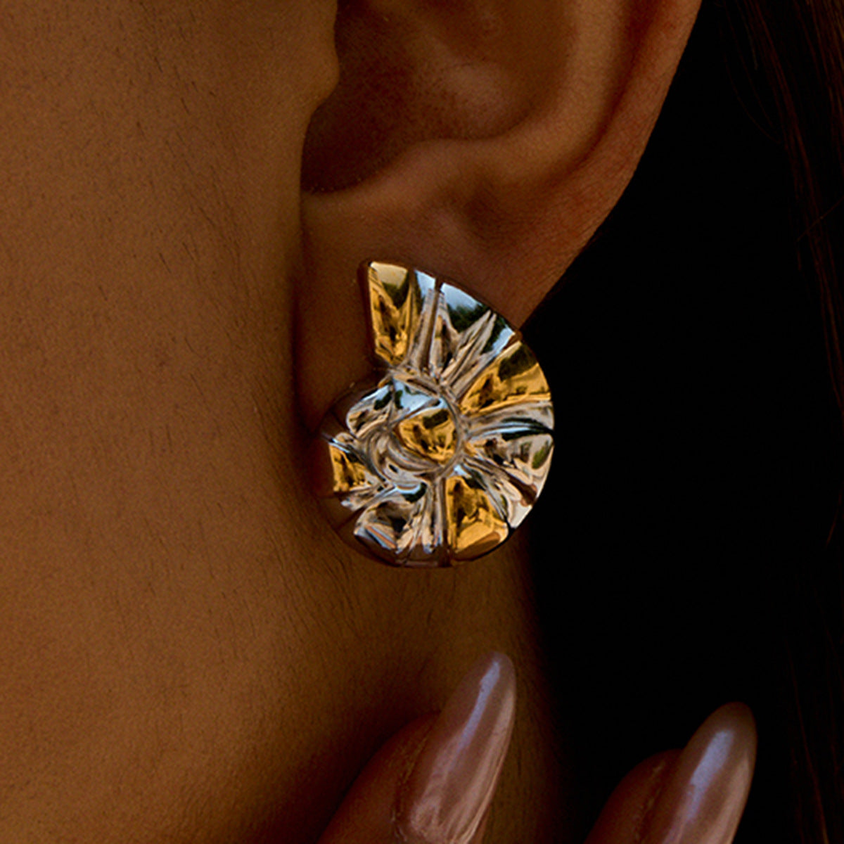 Hand holding silver gold swirl earrings worn on model’s ear