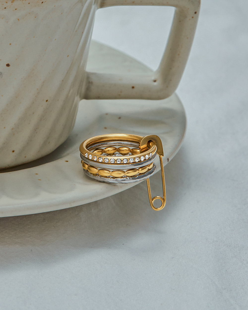 Gold rings stacked on a ceramic saucer with a teacup in the background