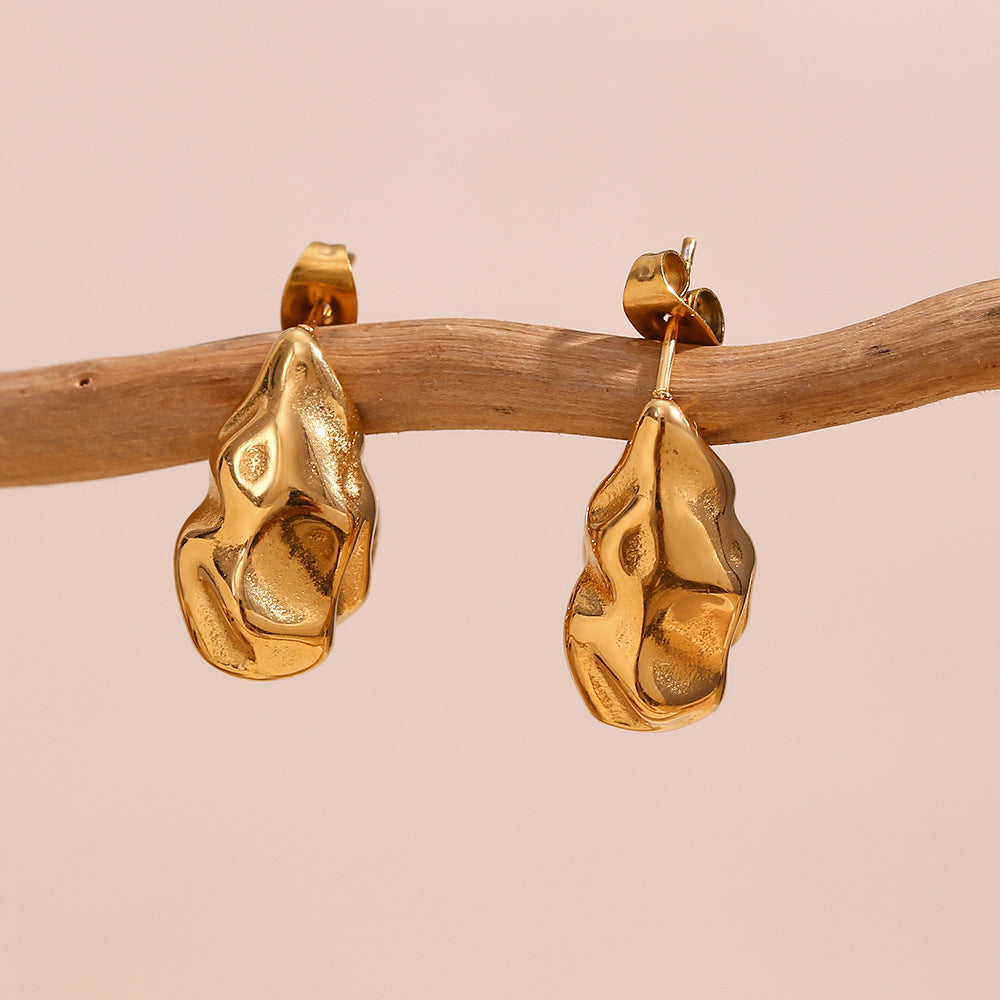 Golden irregular hoop earrings displayed on wooden branch