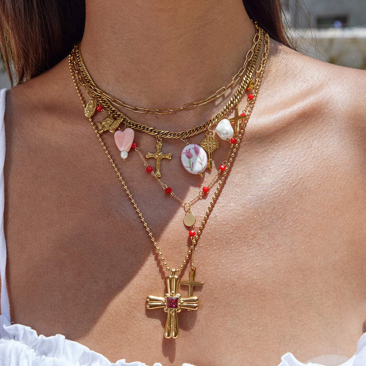 Model layering gold charm necklace with pink heart and vintage cross