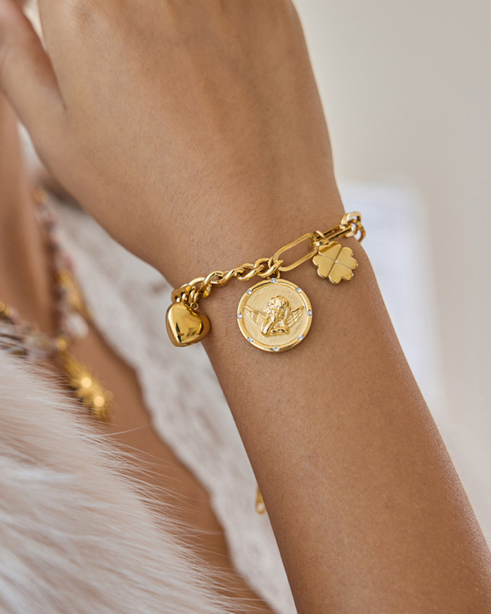 Gold bracelet with charms on a wrist against a neutral background