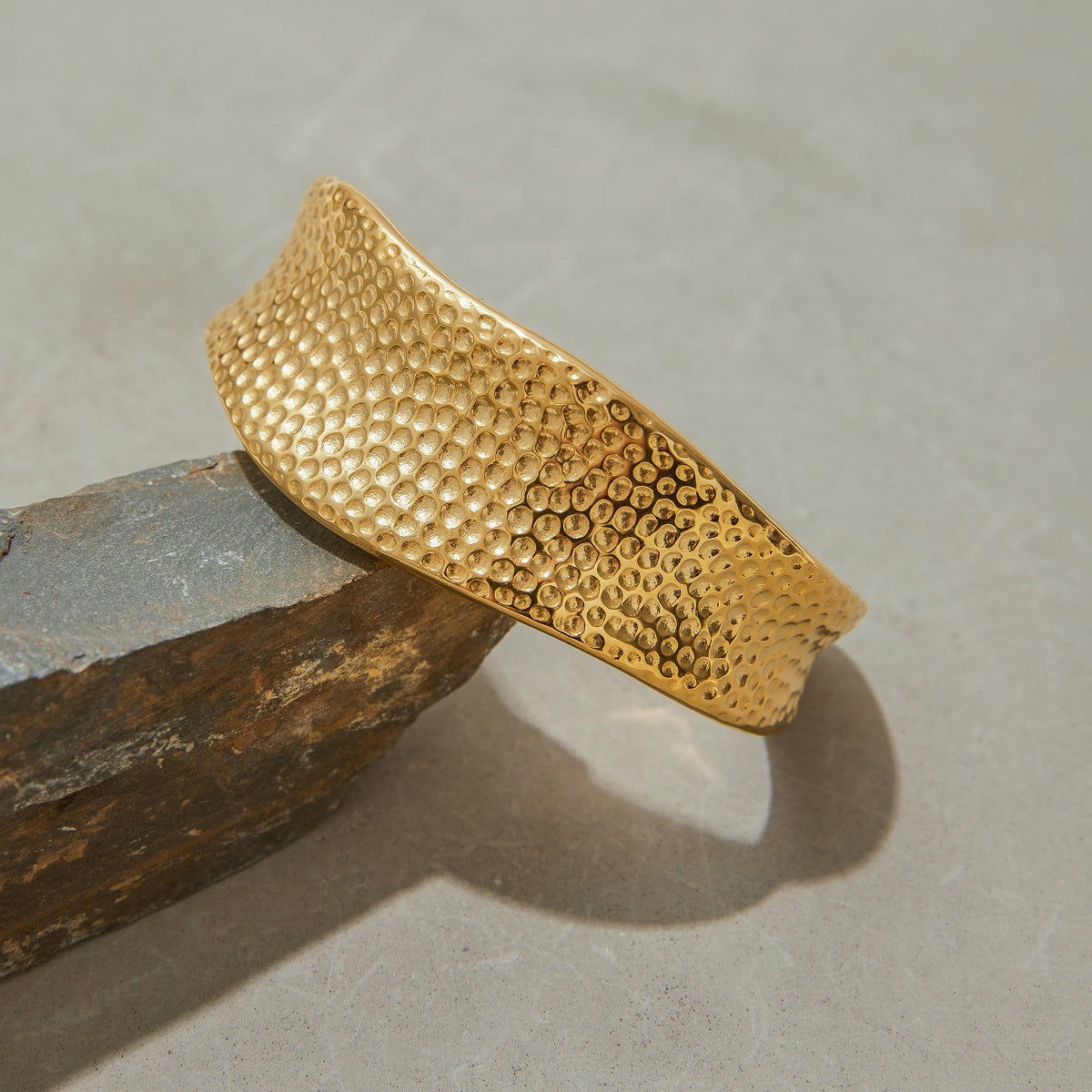 Modern gold bangle bracelet placed on a stone slab, showcasing its shine and textured finish