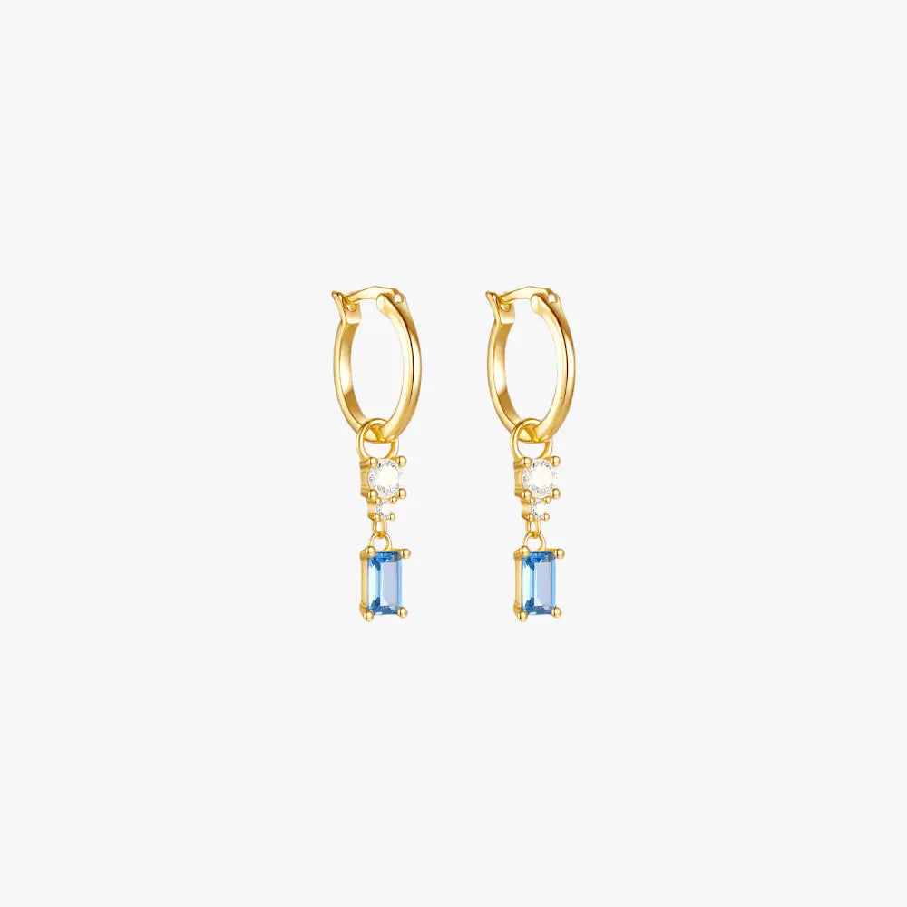 A pair of gold hoop earrings with a blue gemstone and diamond drop.